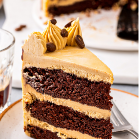 A chocolate layer cake is presented on a white plate with a small cup of espresso next to it.