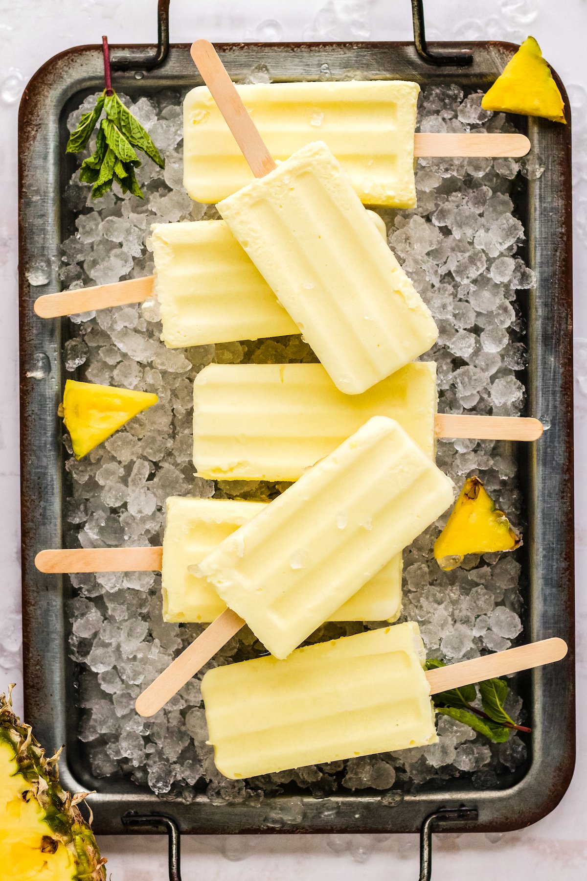 dole whip posicles on a galvanized tray of ice with fresh pineapple