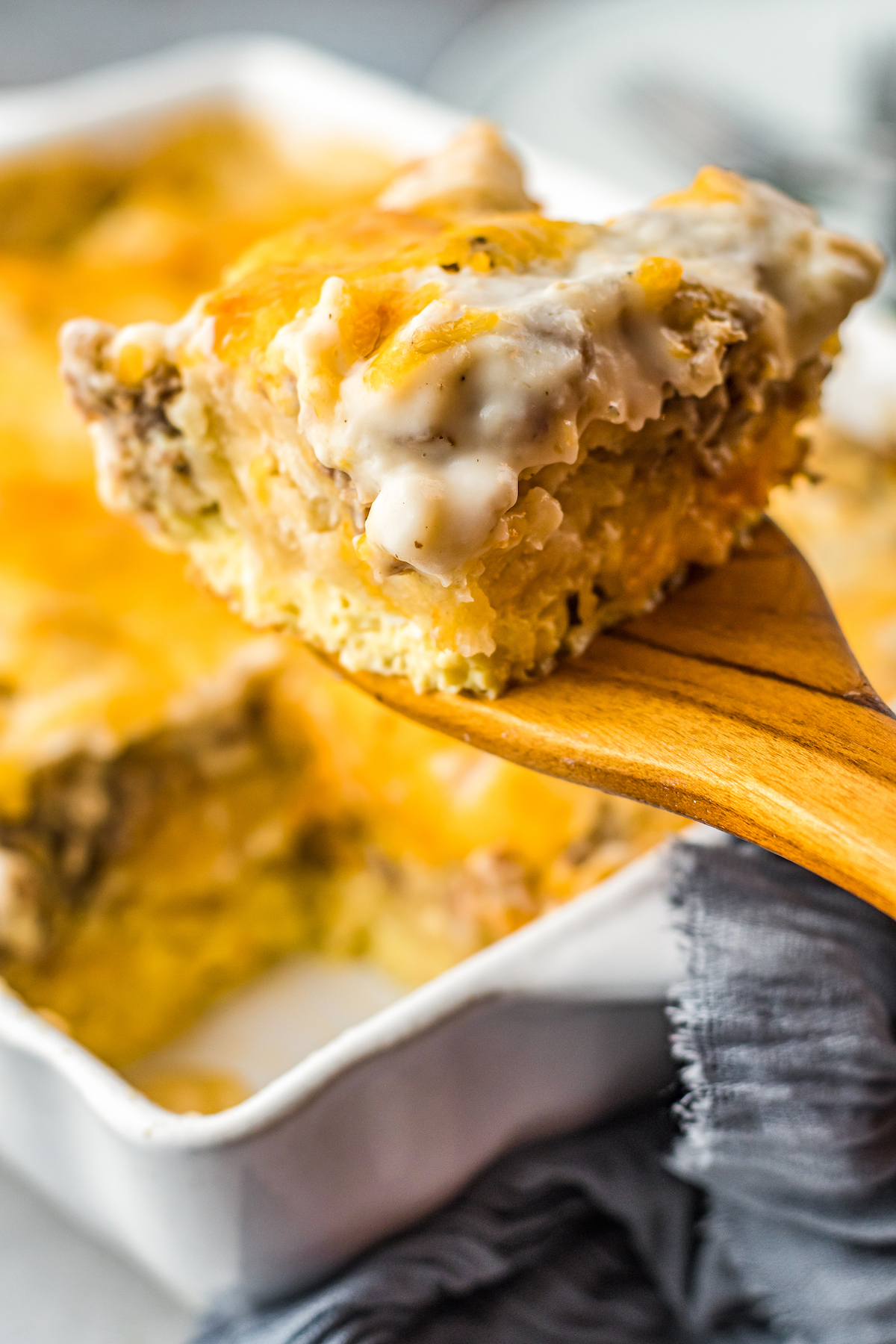 A serving of biscuits and gravy casserole on a wooden spoon being lifted from the breakfast casserole dish.