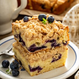 Two pieces of blueberry coffee cake stacked on top of each other on a white plate.
