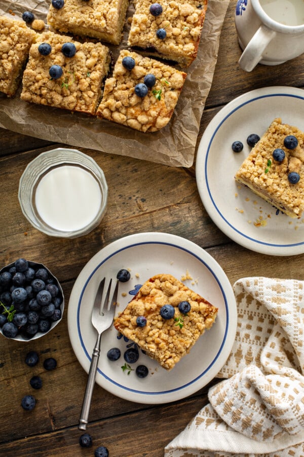 Overhead image of a glass of milk and coffee cake with a fork and coffee cake on parchment paper. 