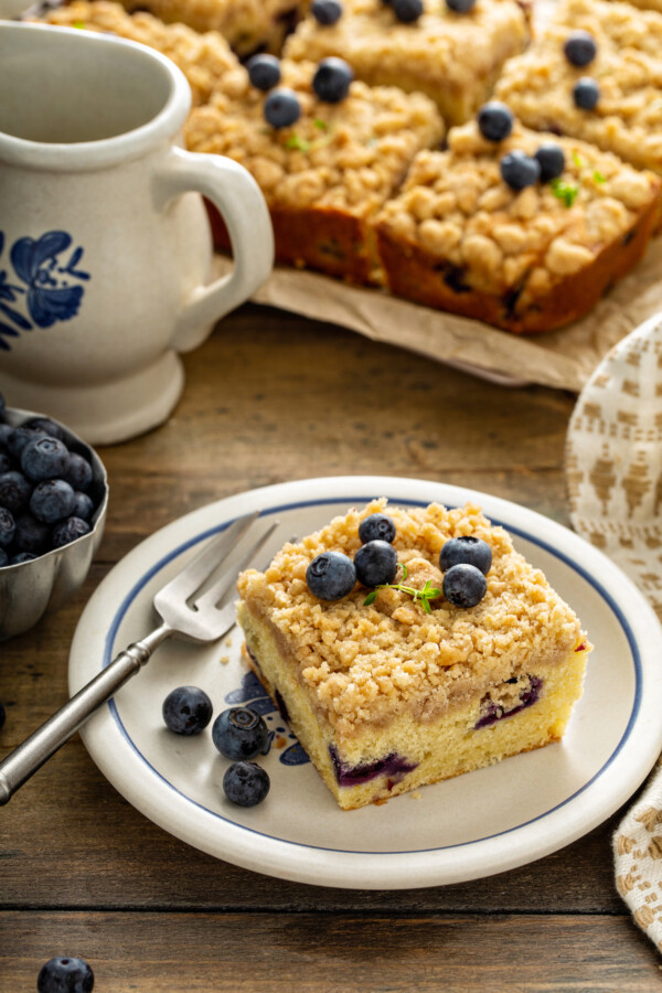 One serving of blueberry coffee cake on a white plate with a fork. 