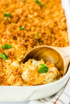 Up close image of cheesy potato casserole in a white casserole dish with a scoop being taken out.