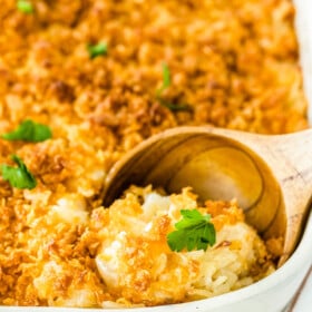 Up close image of cheesy potato casserole in a white casserole dish with a scoop being taken out.