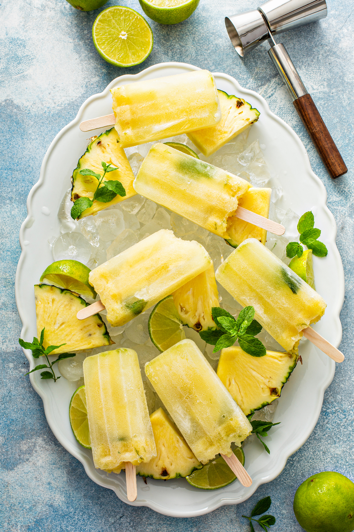 Pineapple Mojito Popsicles arranged on a white plater with ice and mint. 