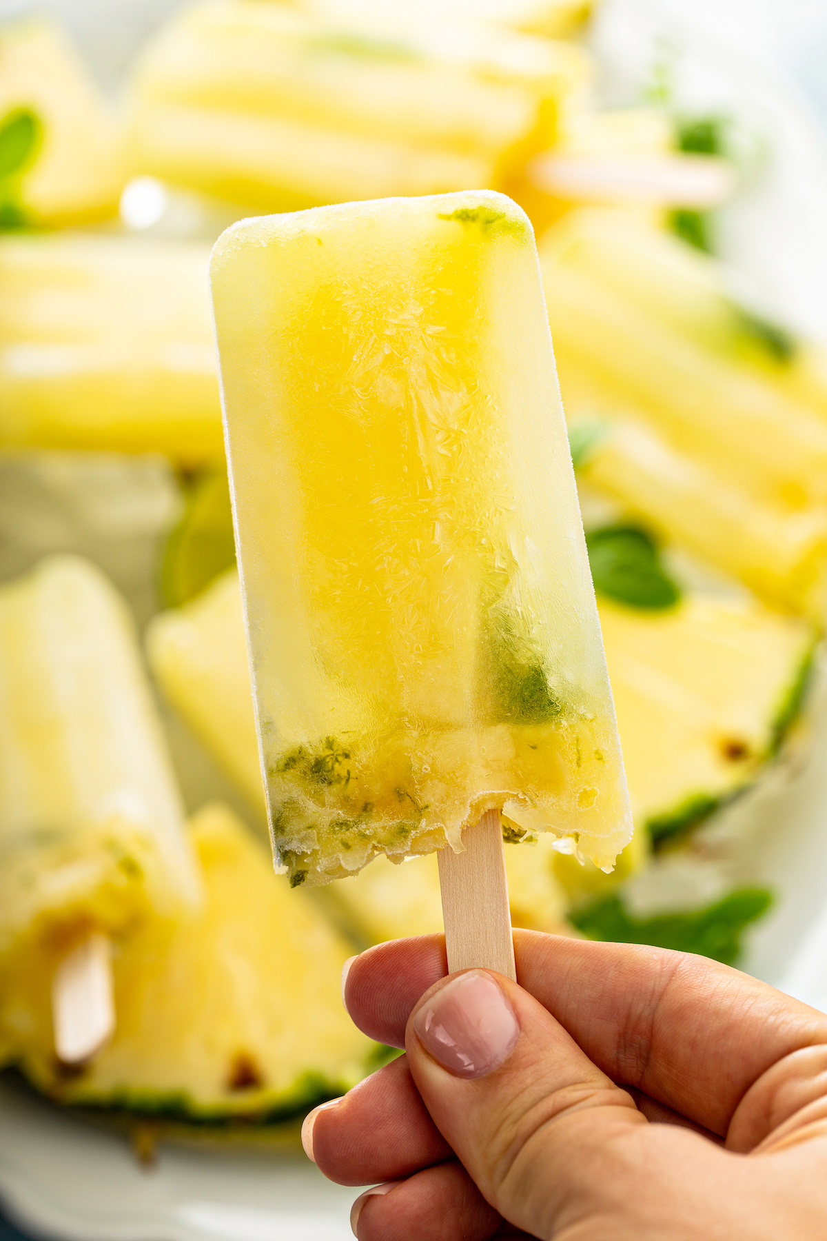 Up tropical image of pineapple mojito popsicle with a hand holding it by the stick. 