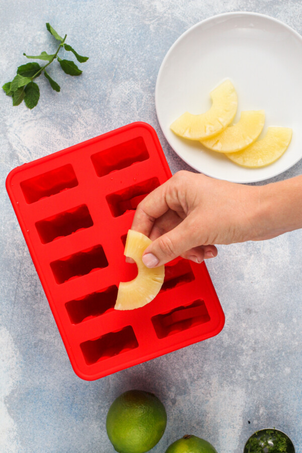 A popsicle mold, a white plate with pineapple slices and mint leaves. 