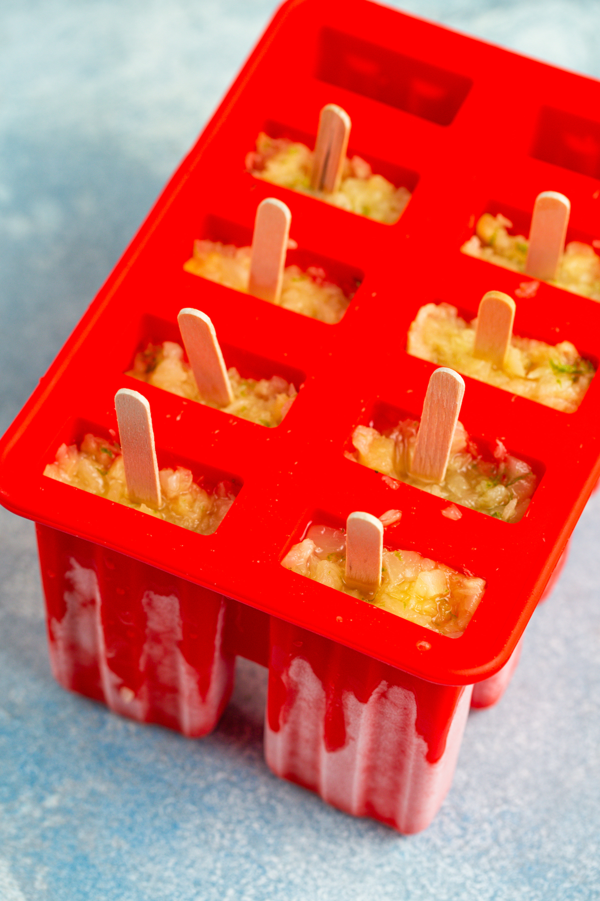 Pineapple popsicle inside molds with popsicle sticks. 