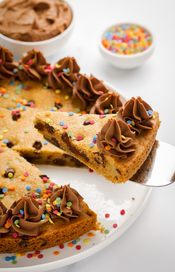 Slice of chocolate chip cookie cake with frosting.