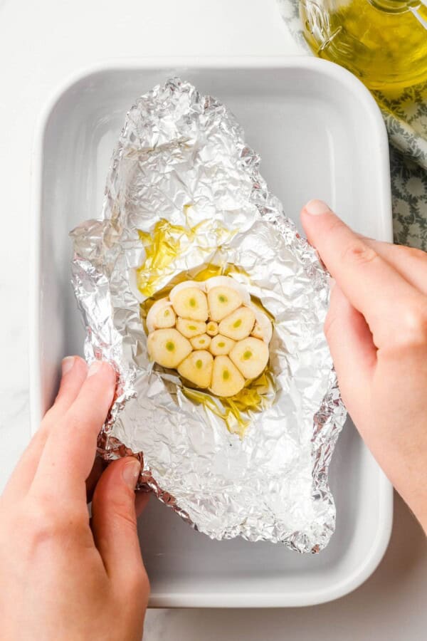 A head of garlic is being wrapped in foil.