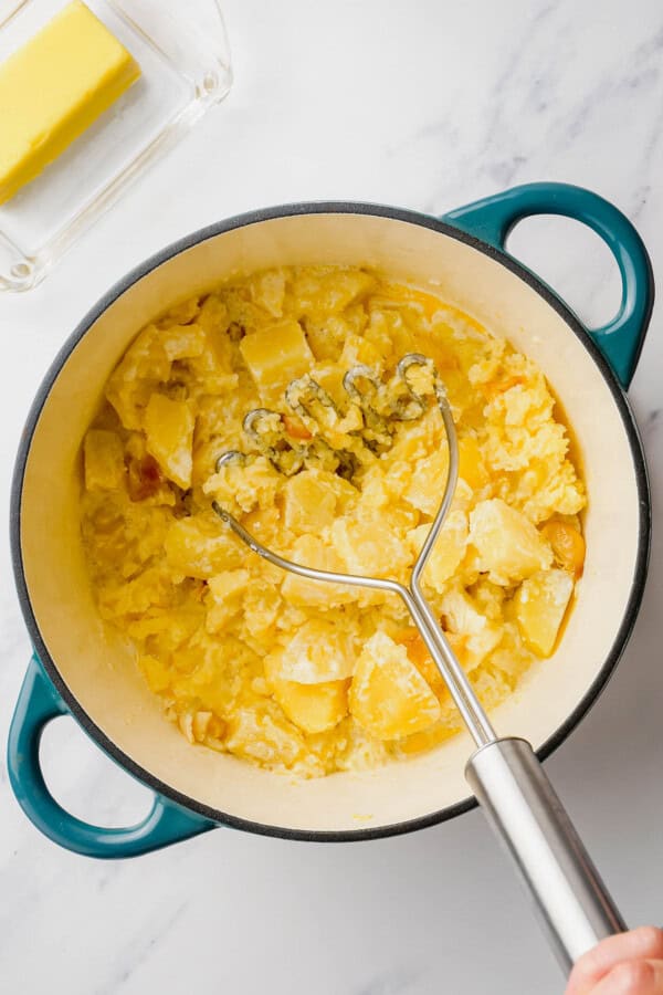 Cooked potatoes are being mashed with a masher.