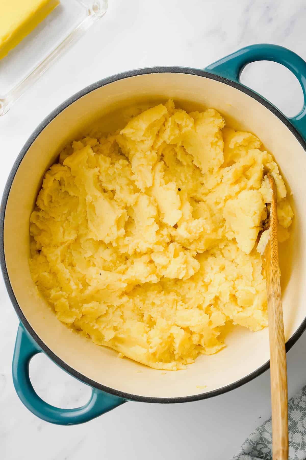 Mashed potatoes are being stirred with a wooden spoon.