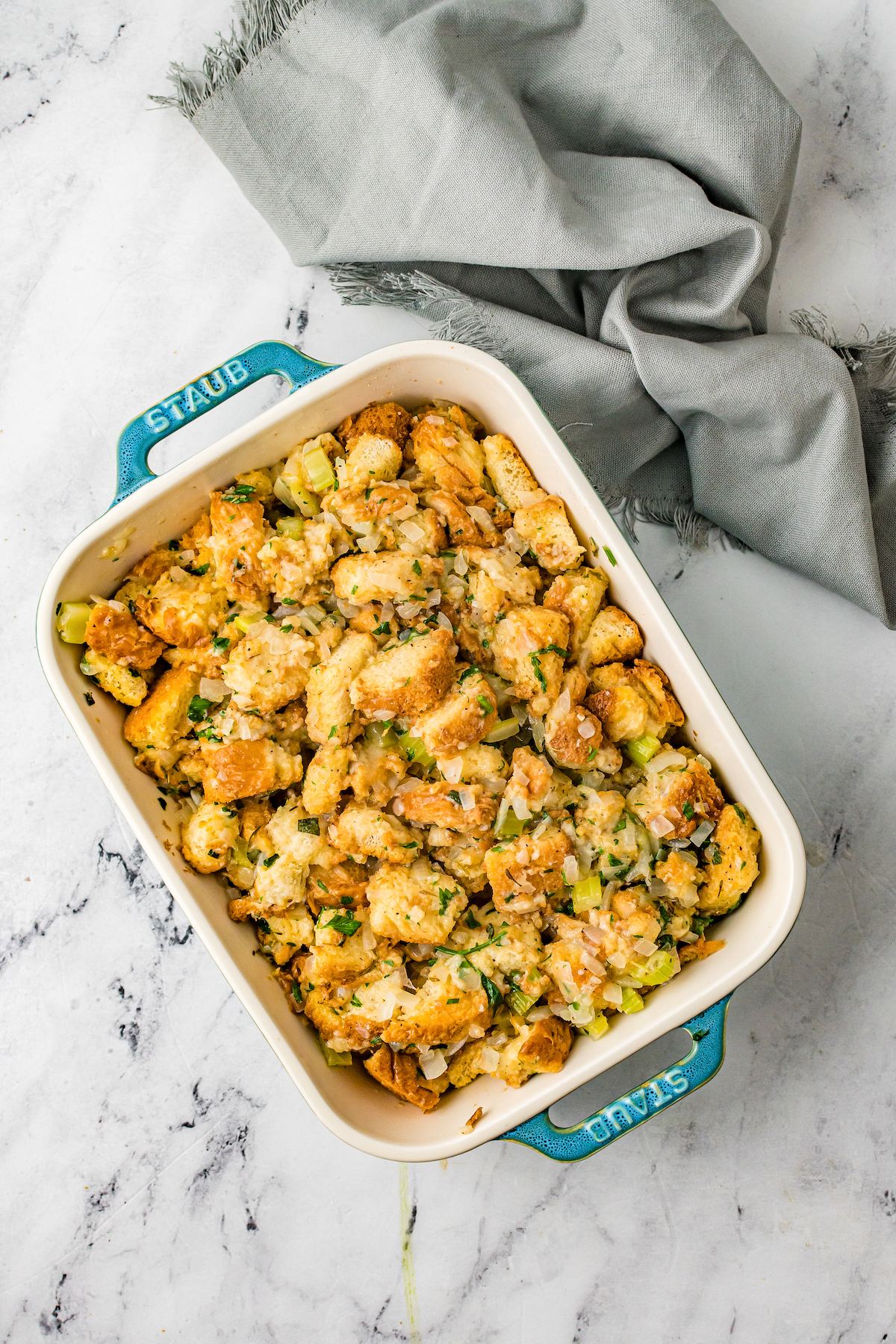 A casserole dish full of Texas toast cubes, celery, herbs, and onion.