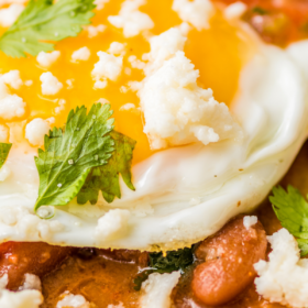 Up close image of a fried tortilla with beans on top and a fried egg.