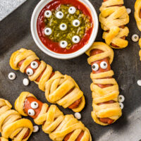 Mummy hot dogs on a baking tray with monster dip.