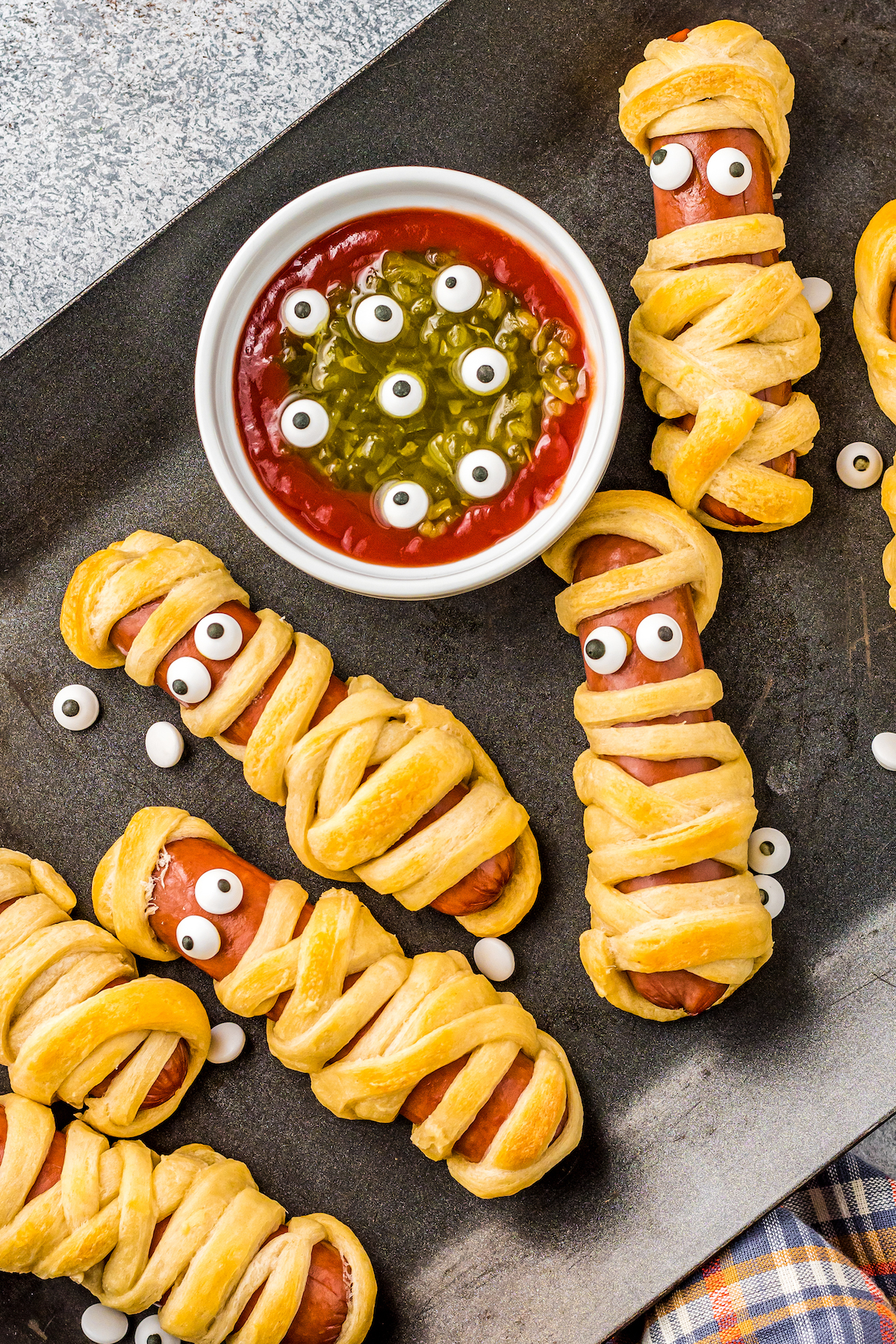 Mummy hot dogs on a baking tray with monster dip.