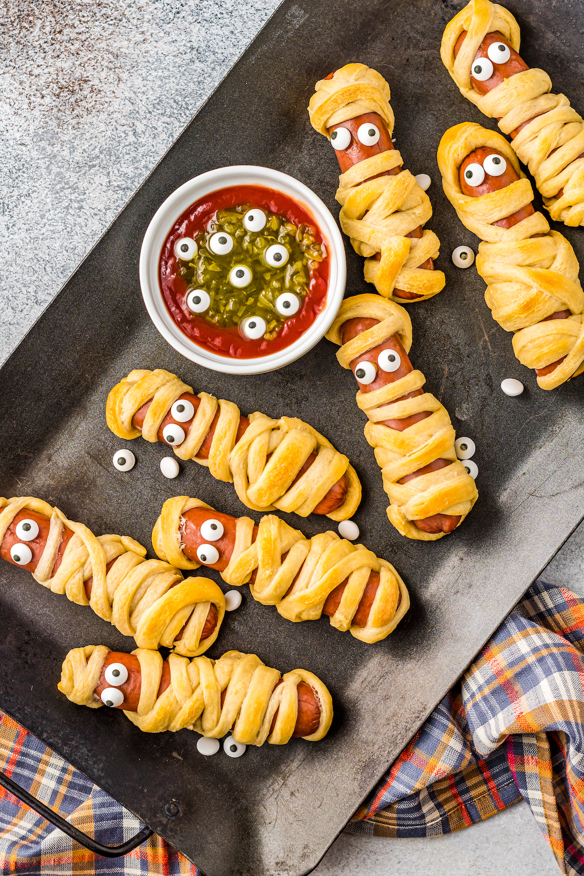 Mummy hot dogs with a bowl of ketchup and relish.