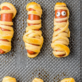 Mummy hot dogs on a baking sheet with one mummy hot dog with eyeballs.
