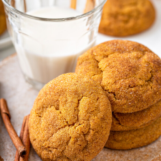 Stack of pumpkin cookies next to a glass of milk.