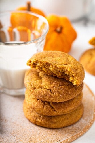 Pumpkin cookies in a stack next to a glass of milk.