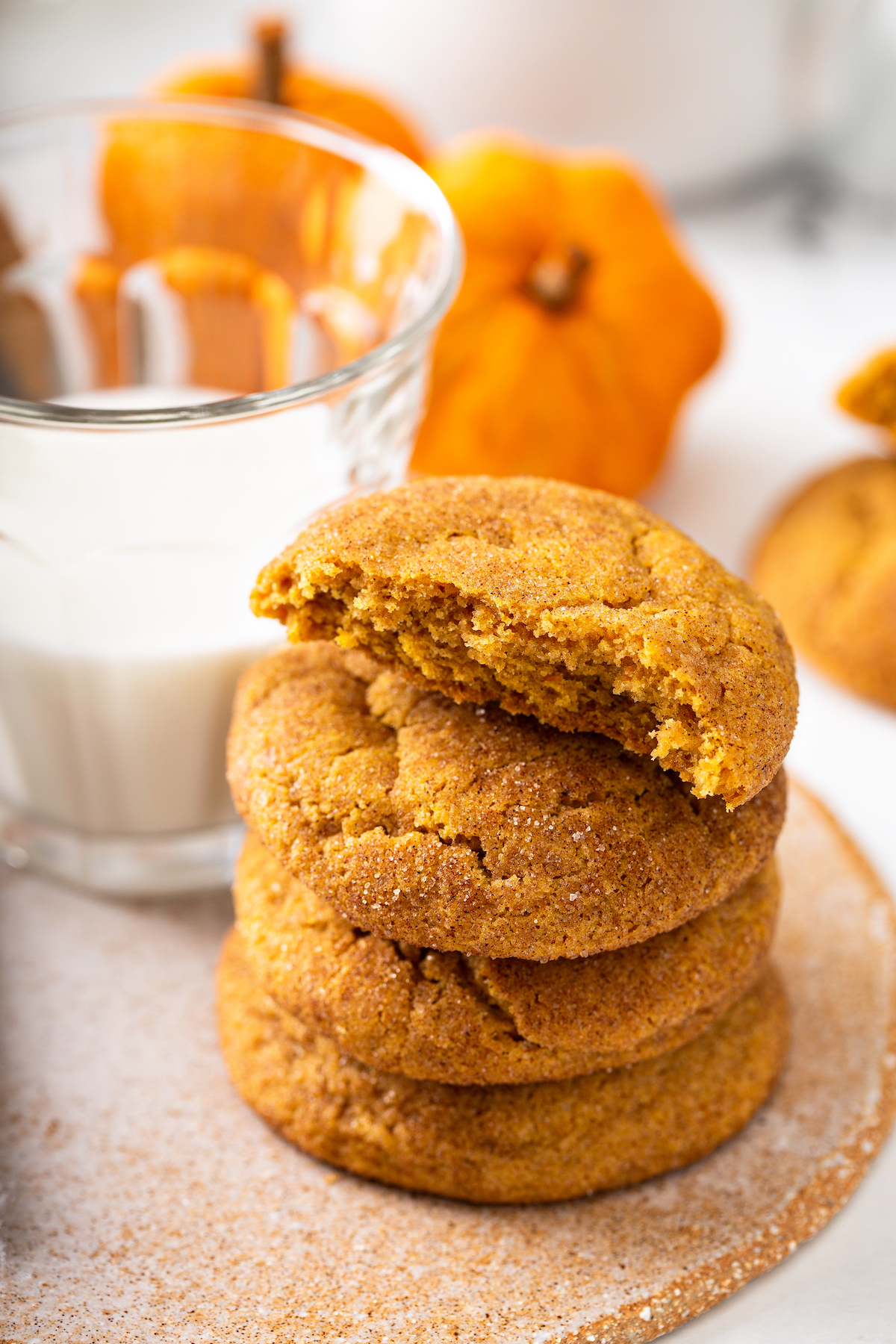 Pumpkin cookies in a stack next to a glass of milk.