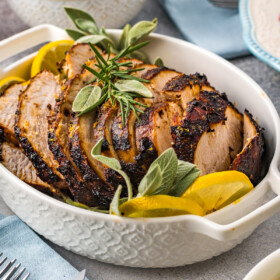 A serving dish filled with sliced turkey breast, lemon slices, and herbs.