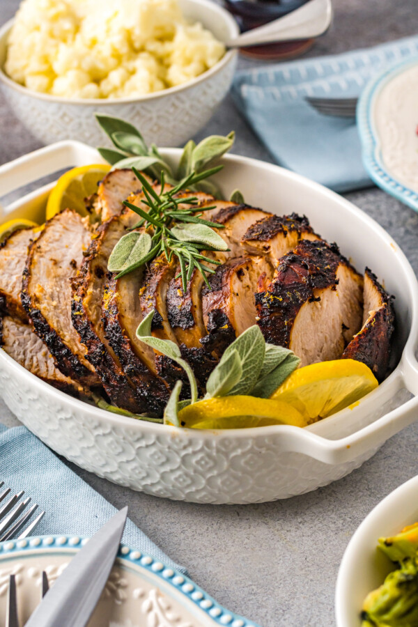 A serving dish filled with sliced turkey breast, lemon slices, and herbs.