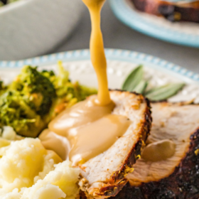 Sliced air fryer turkey breasts on a plate with brown gravy being poured on top.