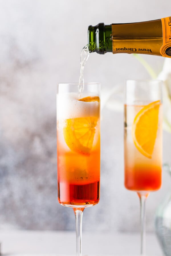 Champagne being poured into a glass containing Aperol and a sliced orange.