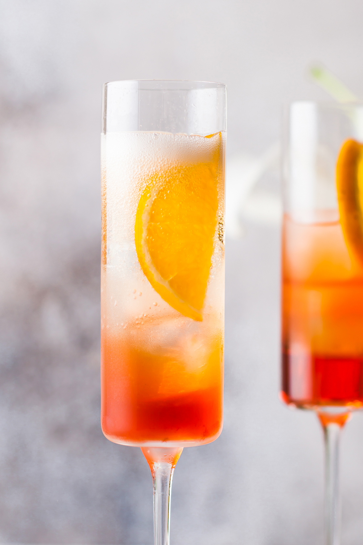 Close-up shot of two Aperol spritzes, with orange slices in the glasses against the sides of the glasses.