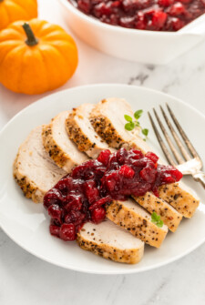 A plate with slices of roast turkey topped with cranberry sauce.