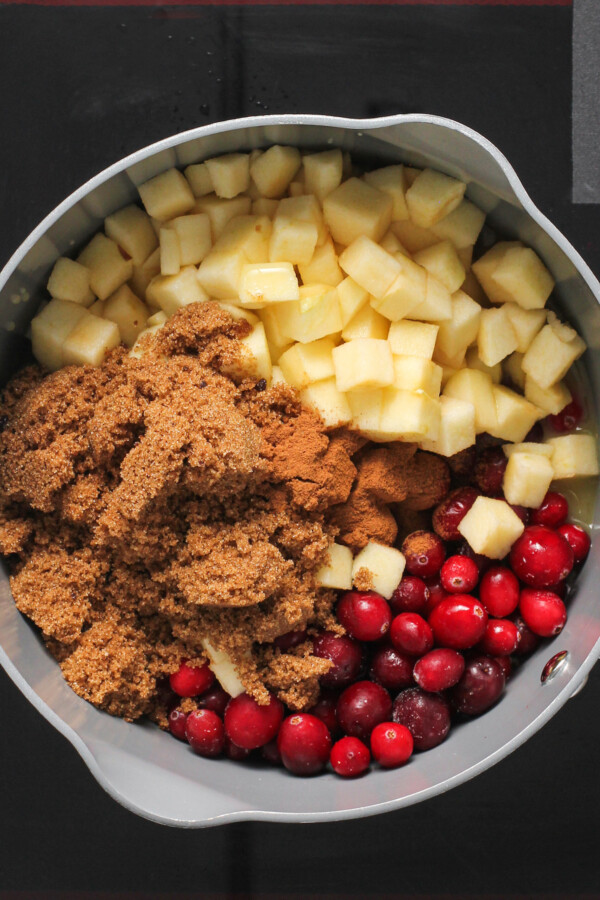 A saucepan with uncooked chopped apples, cranberries, and brown sugar inside.