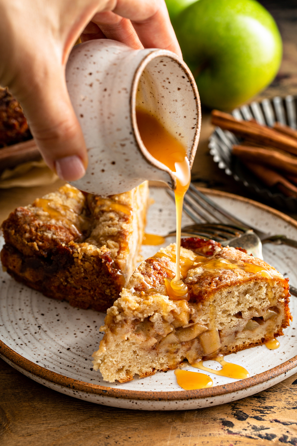 Two slices of Apple Streusel Cake on a white plate with caramel sauce being drizzled on top of one slice of cake.