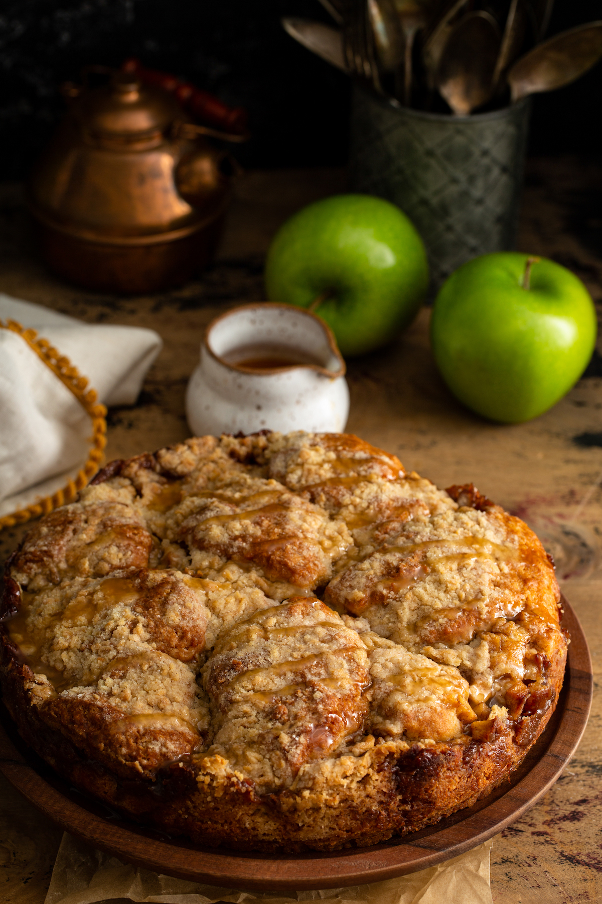 Whole Apple Streusel Cake on a brown wood platter with caramel drizzled on top.