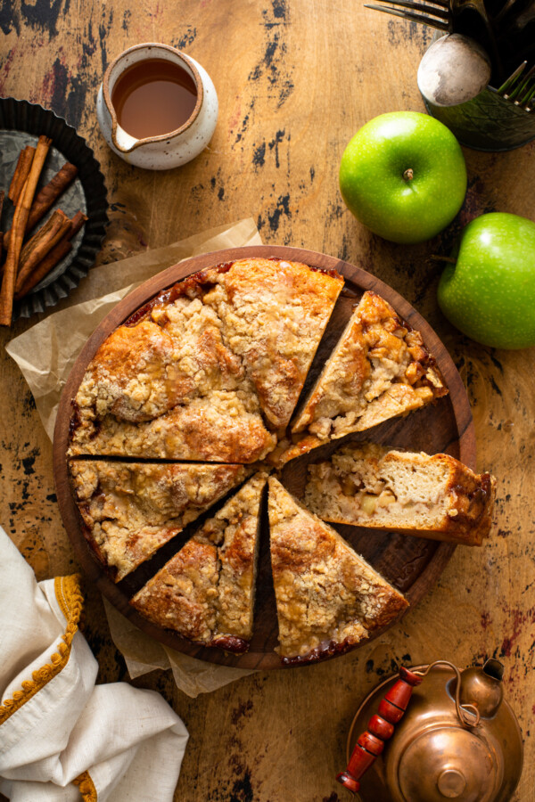 Overhead view of a sliced Apple Streusel Cake on a wood platter with apples and caramel around.