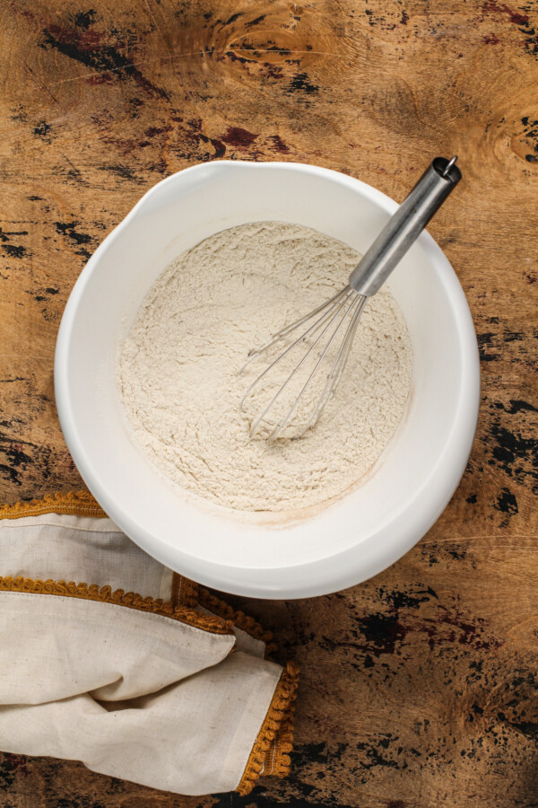 Dry ingredients in a white mixing bowl with a whisk and a tea towel.
