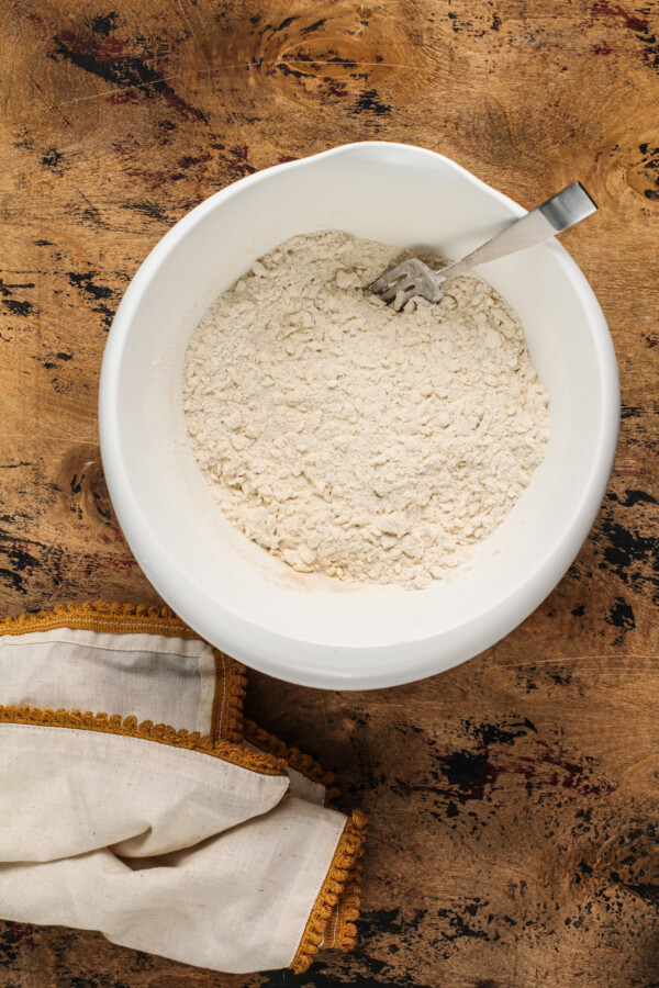 Flour in a white mixing bowl with a fork and a tea towel.