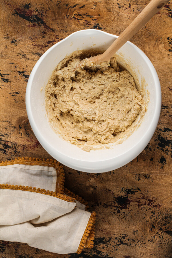 Cake batter in a white bowl with a wooden spoon and a tea towel.