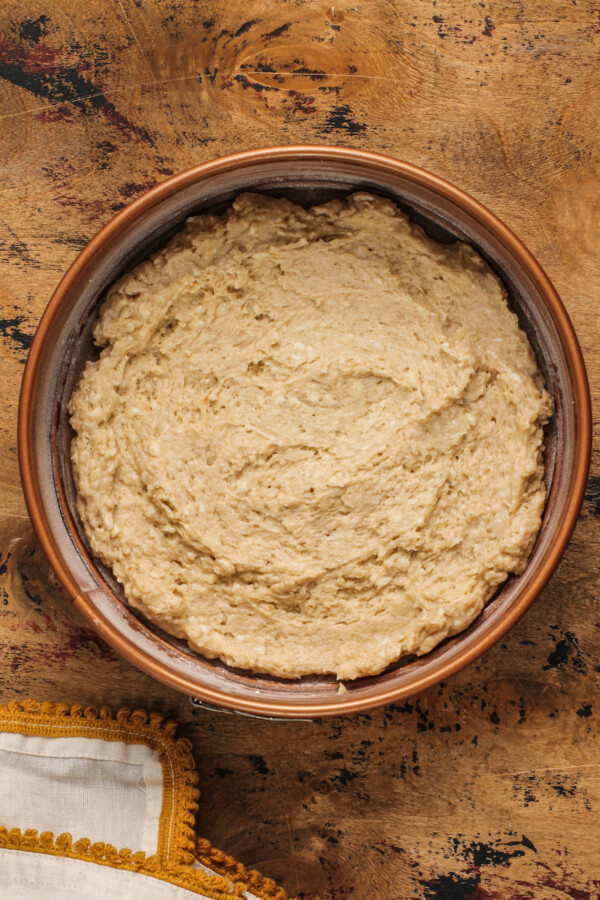 Apple cake batter in a round baking dish with a tea towel.