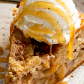 A slice of Apple Streusel Cake on a white plate with caramel on top.