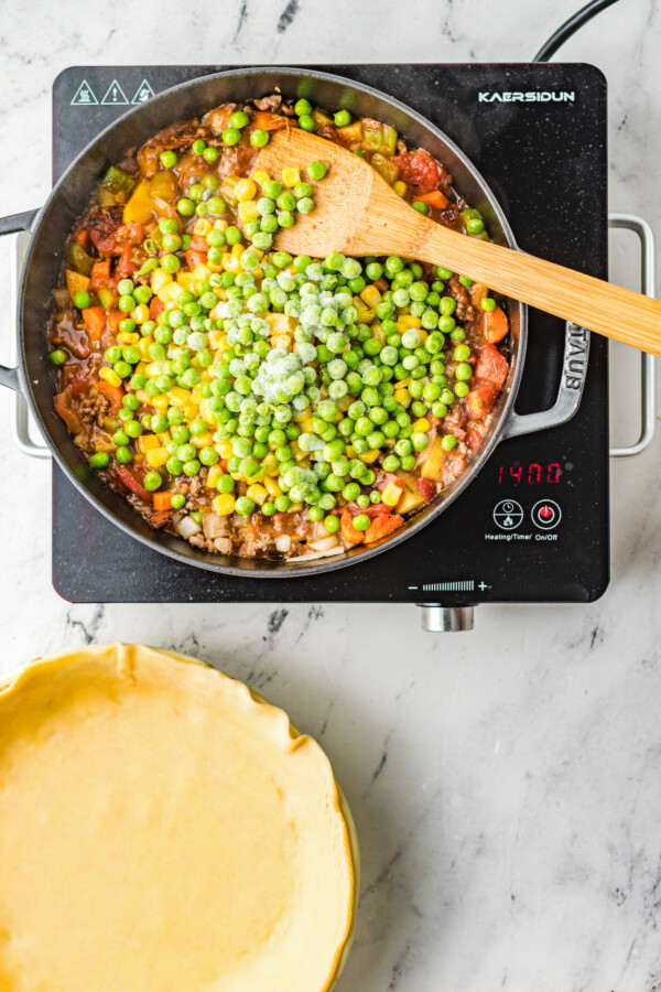 Ground beef with corn, peas, potatoes, onions, celery, and other ingredients in a skillet.