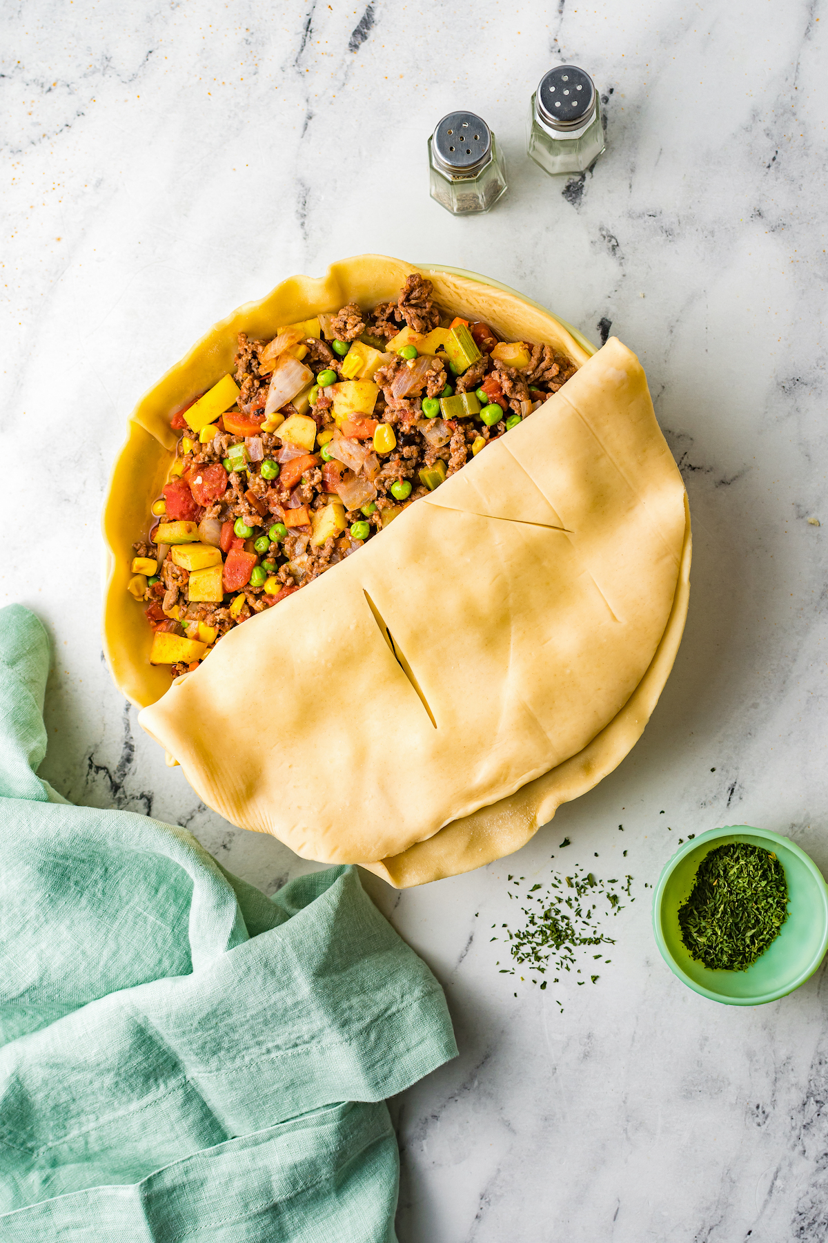 A filled pot pie crust with the top crust halfway on.