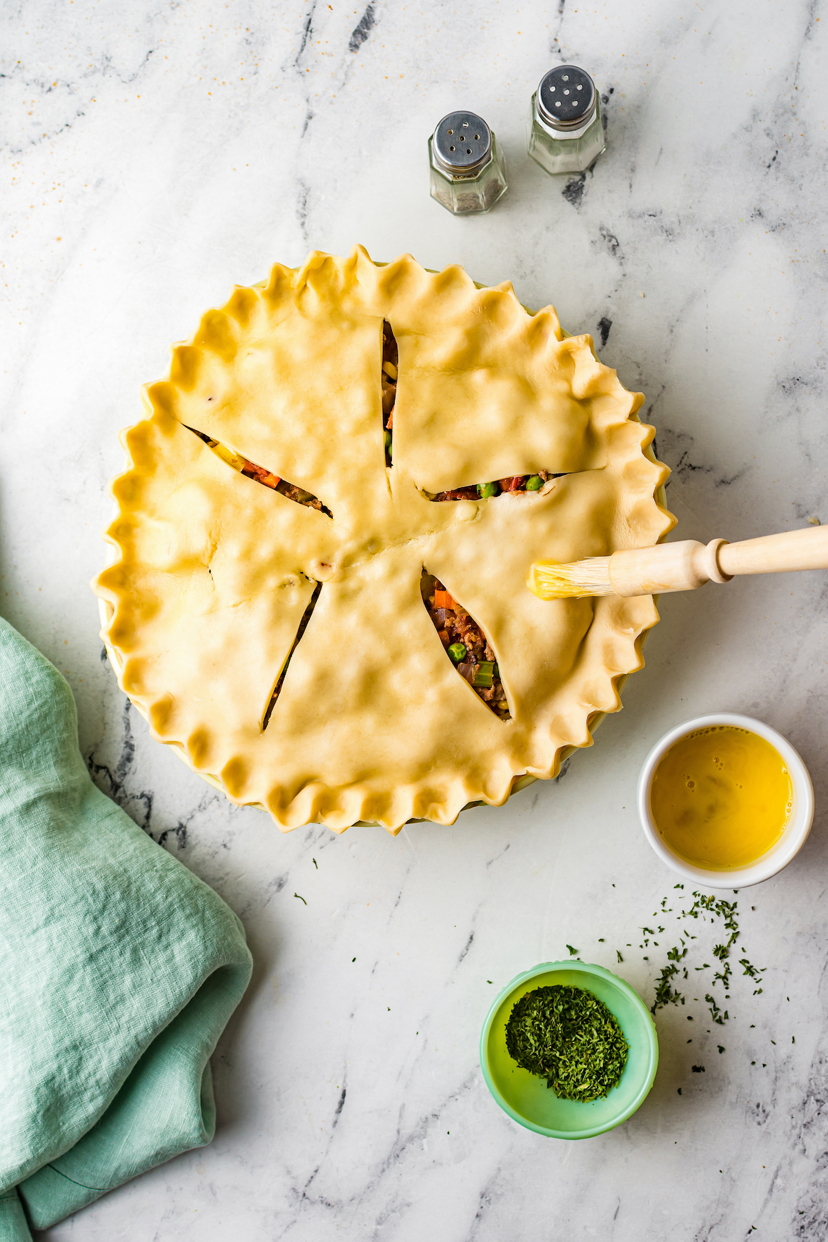 A filled pot pie with top crust in place and edges crimped. Egg wash brushed on.