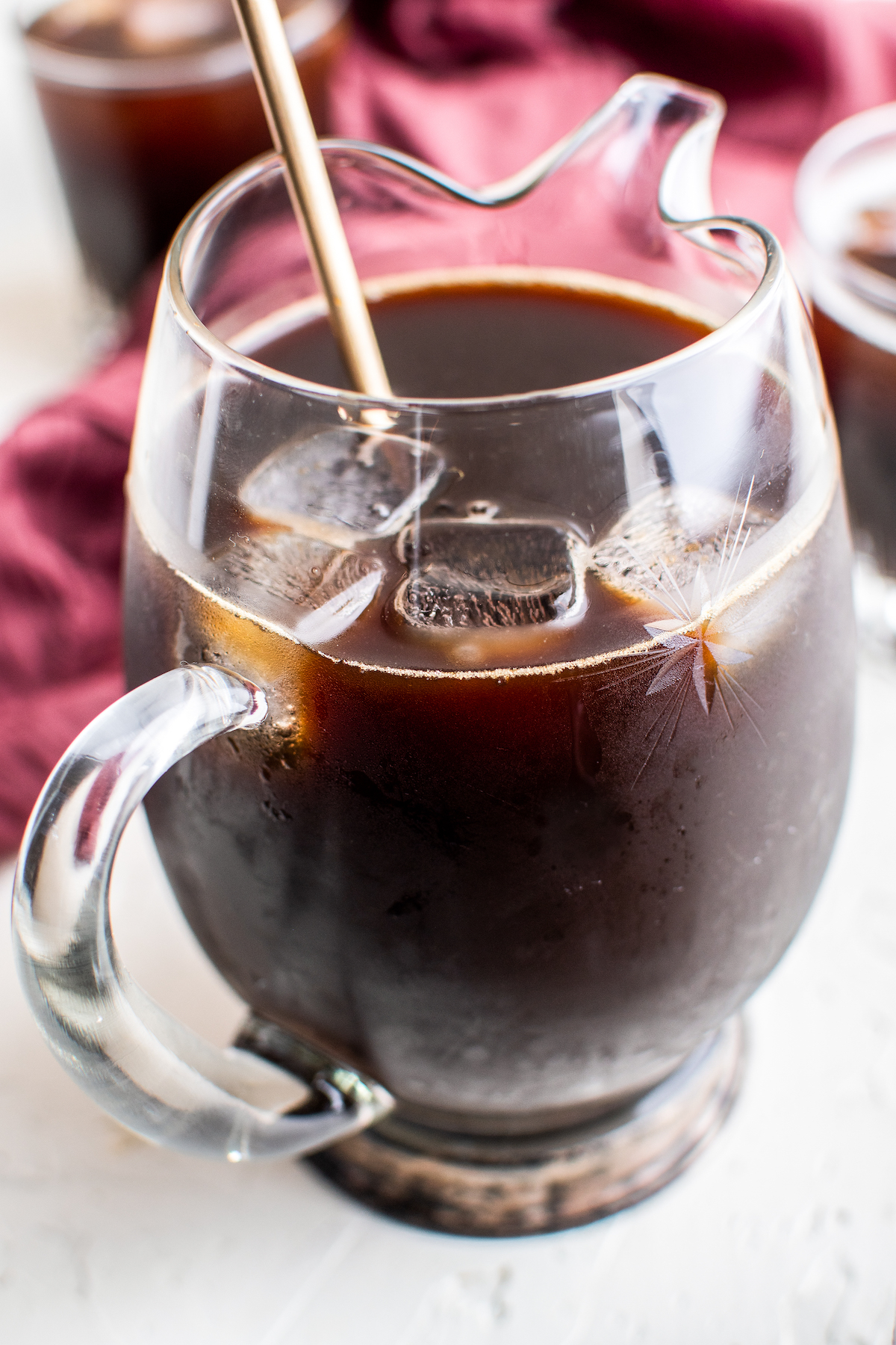 A clear glass cocktail pitcher filled with coffee, liqueur, and ice with a golden stirrer.