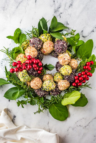 A cheese ball wreath decorated with floral stems and fresh herbs.