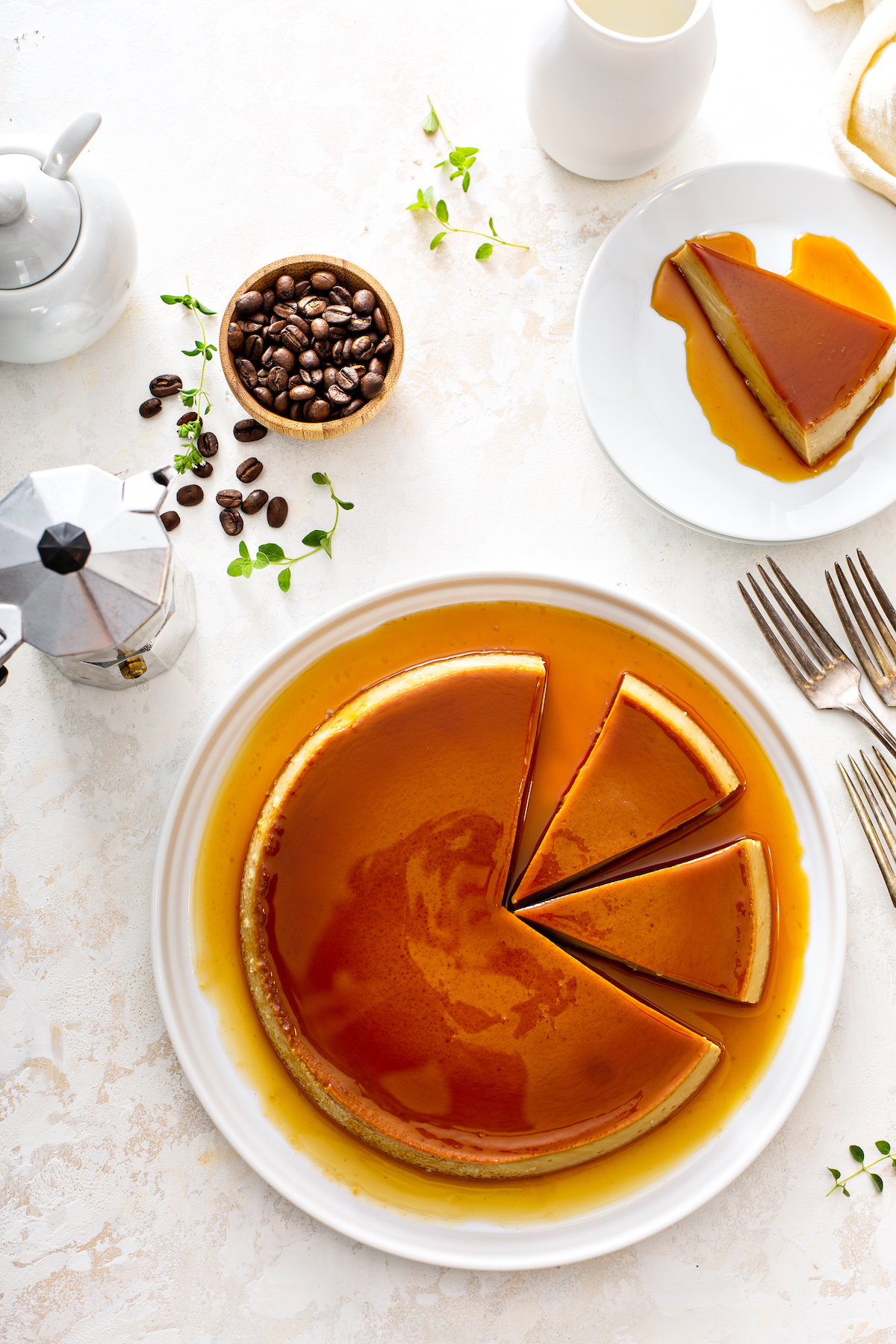 A slice of coffee flan on a white plate and an entire flan on a large white serving platter with coffee beans around.