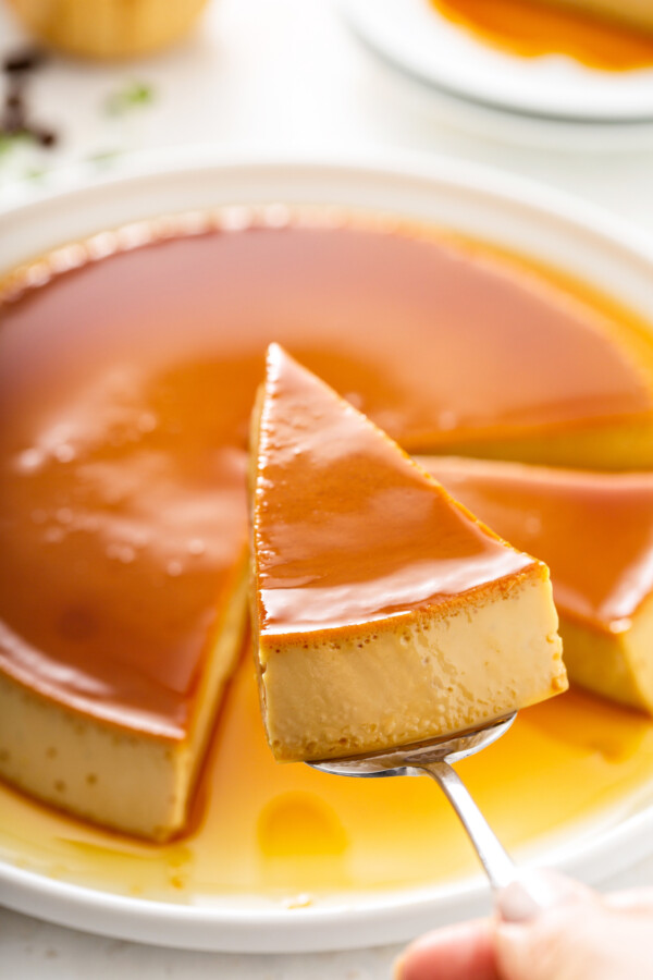 Coffee flan on a plate with a slice being lifted with a cake serving tool.