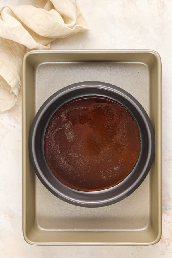 Overhead view of a flan pan in a larger baking pan on a stone background.