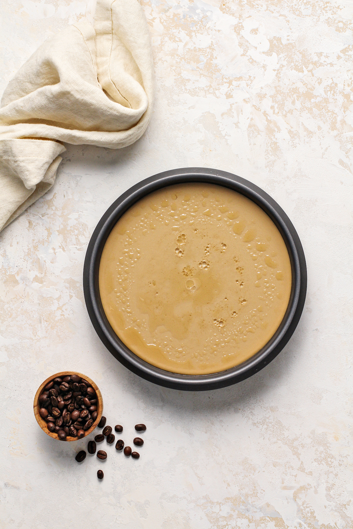 Freshly baked flan that has been chilled still in a baking pan with espresso beans in a bowl.
