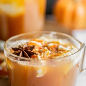 Image of pumpkin apple cider in a glass mug with whip cream.